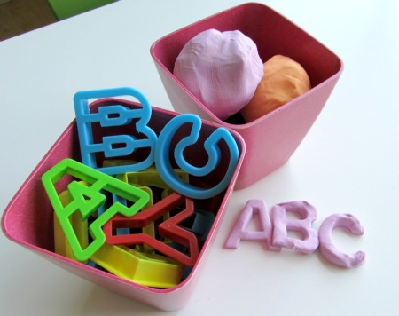 Plastic letter shapes and a bin of different color playdough, with letters ABC in pink playdough as an example 