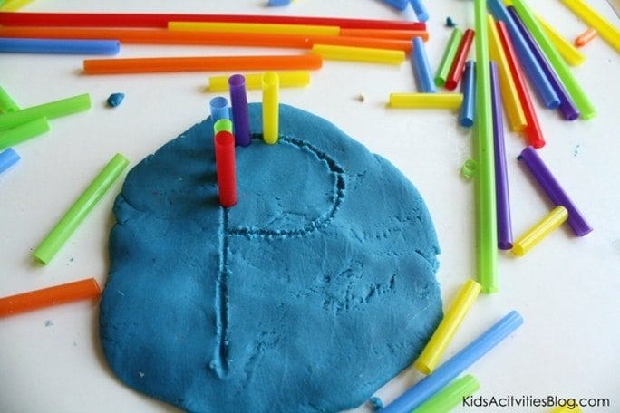 Blue playdoh with the letter P scraped into it. Colorful straw segments stuck into the the outline of the letter and on the table next to it. 