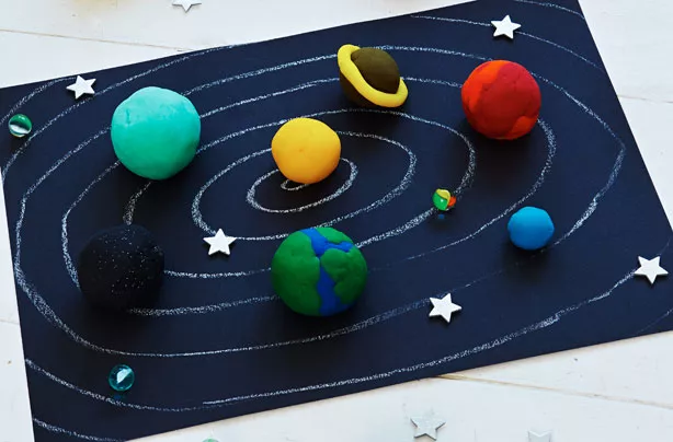 planets are made from play dough. They are on a black piece of paper with white swirls drawn on to be the solar system.