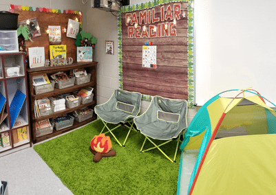 A classroom is shown with a green rug and a plush, toy campfire on it. Camping Classroom Theme