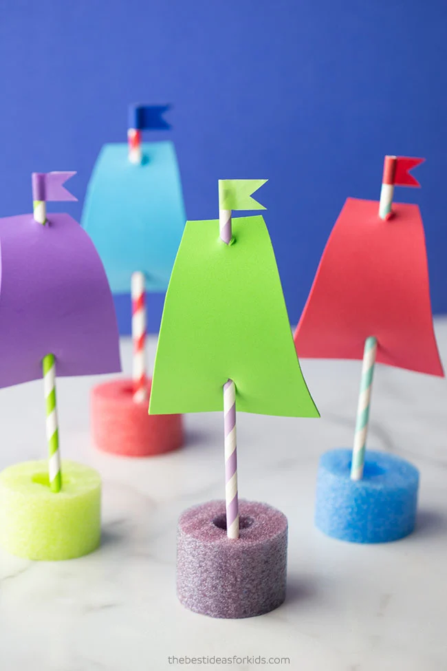 Easy crafts for kids include these pool noodle boats made from a small piece of a pool noodle with a straw coming out of it. A piece of foam is attached to the straw to act as a sail.