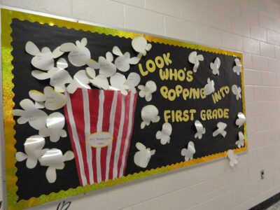 Back to school bulletin board idea that says "look who's popping into first grade" with a huge popcorn container and popcorn pieces flowing out. 