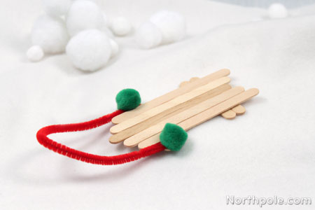 Five popsicle sticks glued together to form a mini sled with a pipe cleaner and pom pom handle