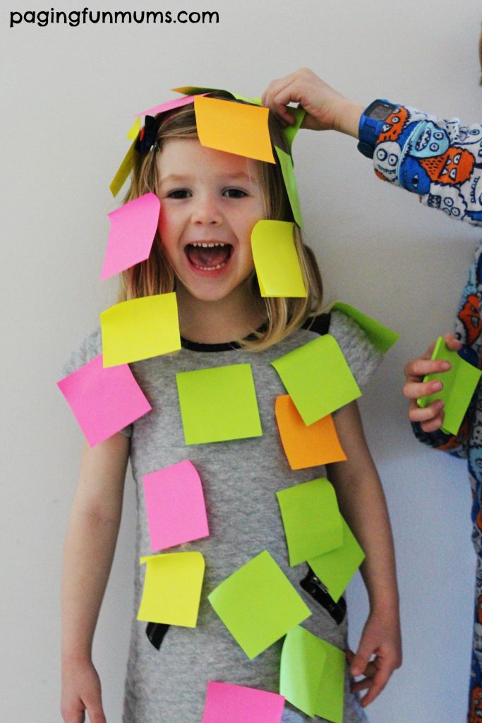 A little girl is covered in post it notes in this example of minute to win it games.