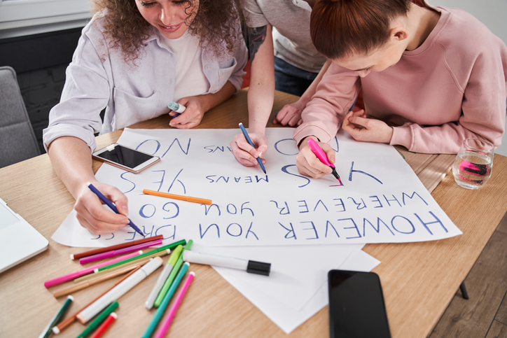 Two girls are shown making posters with markers and posterboard in this example of pep rally activities.