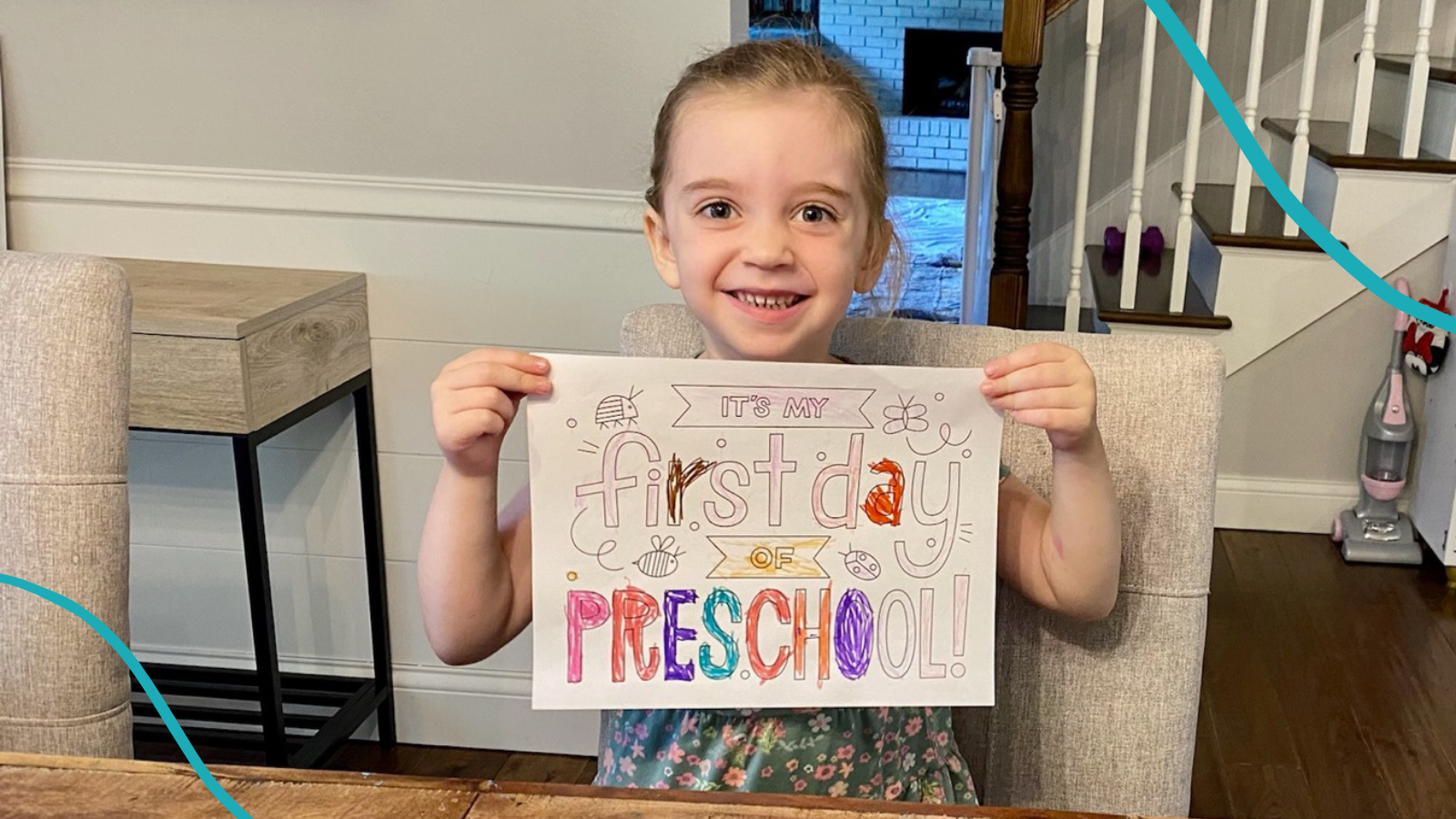 Girl sitting at table at home holding a sign that says First Day of Preschool