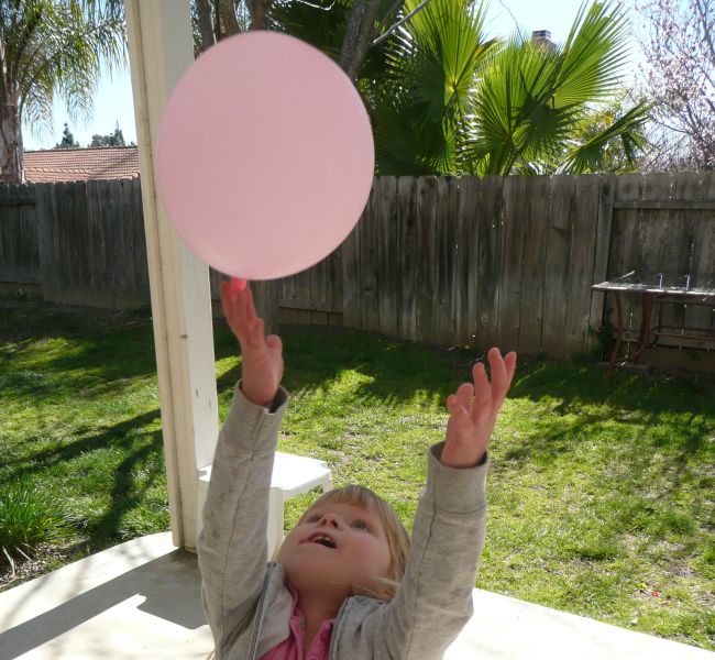 Toddler throwing a pink balloon into the air