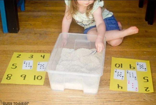 Preschooler digging through a container of sand to find playing cards to match numbers (Preschool Math Games)