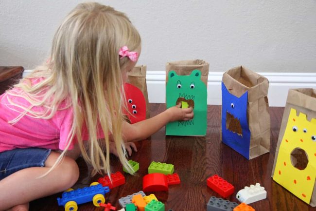 Toddler sorting LEGOs into paper bags decorated to look like monsters