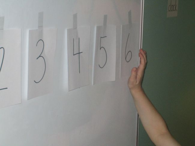 Toddler tapping the number six taped to a wall as part of a row of numbers (Preschool Math Games)