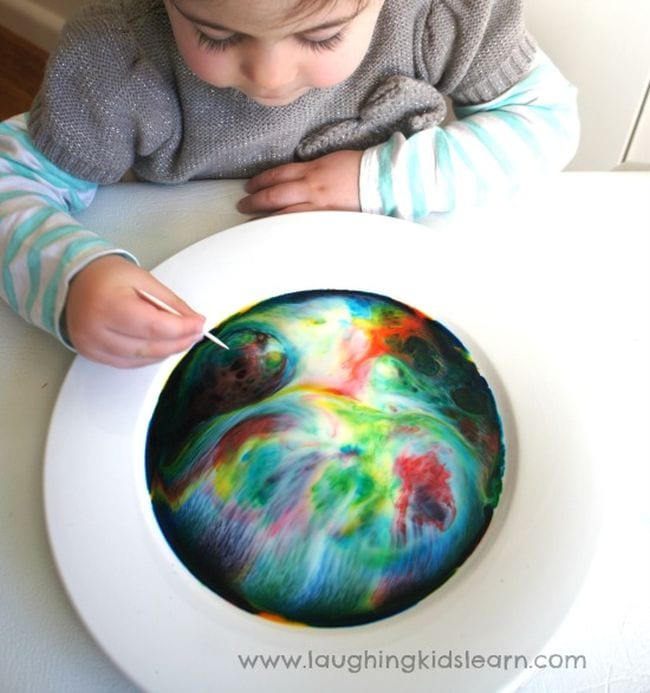 Preschool science student mixing a bowl of colorful milk swirls