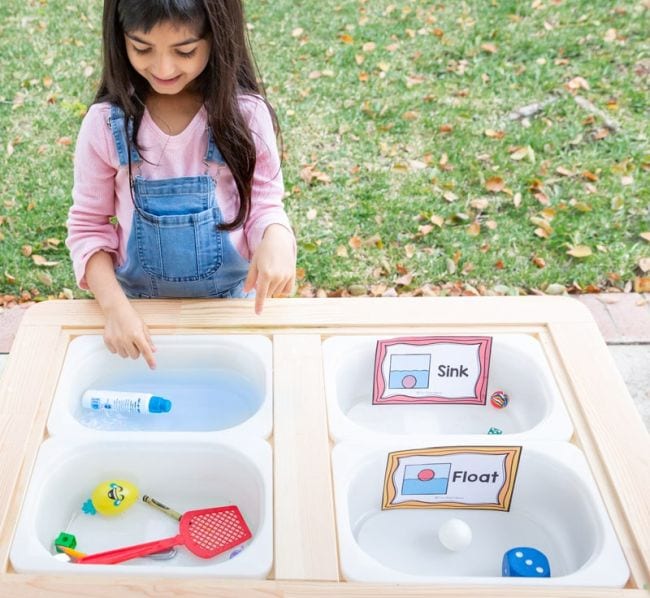 Preschool science student placing objects in bins of water to see if they sink or float