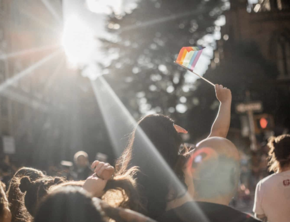 Woman holding up pride flag in crowd- Pride Month activities