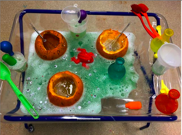 Classroom water table with hollowed pumpkins, colored soapy water, utensils and colored plastic bottles for potions sensory play ideas for the classroom 
