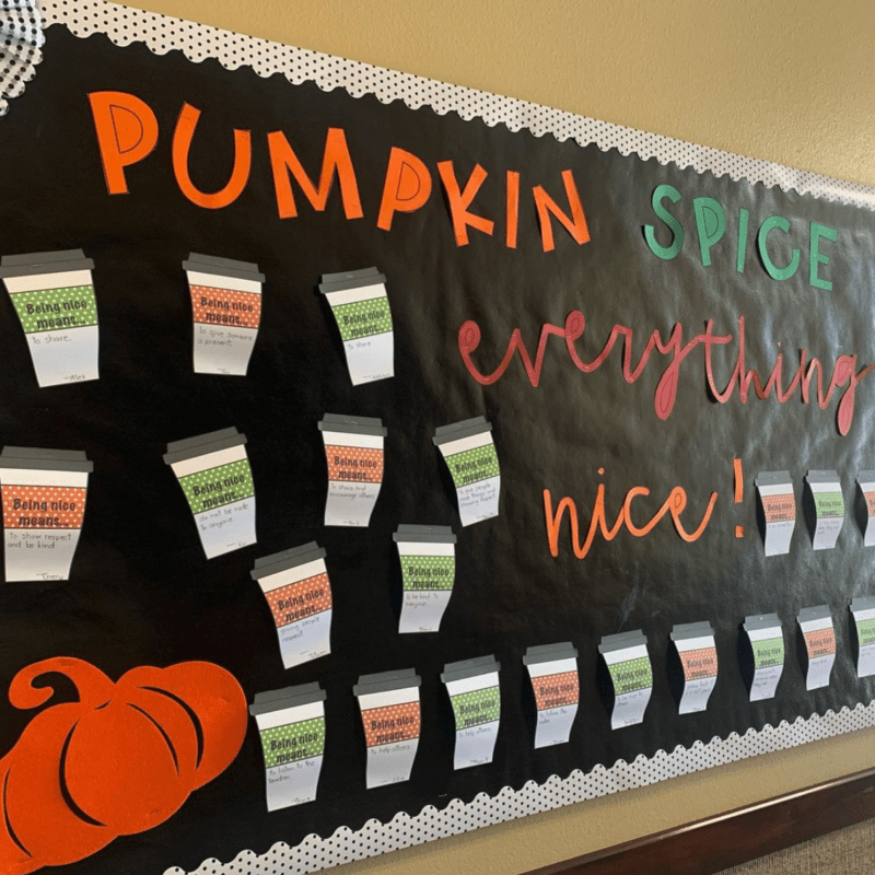 A black background has orange, green, and red text that says pumpkin spice and everything nice. There are disposable coffee cups with lids all over the board.