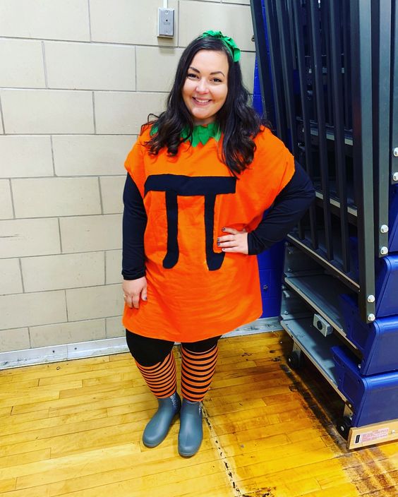 A woman is shown wearing an orange shirt with a green collar to look like a pumpkin. The mathematical symbol pie is on the shirt.