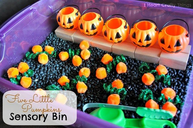 Several small pumpkin containers are lined up in the back of a bin with small orange pumpkins in pretend dirt in front of them. (fine motor activities) 