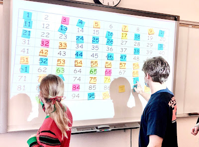 Two students stand in front of a white board with colorful sticky notes on it
