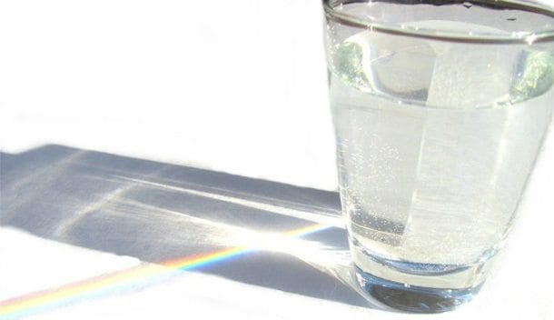 sunlight reflecting through a glass of water, creating a rainbow on the table behind