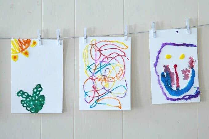 Three paintings are hung from a clothes line in this example of kindergarten art projects.