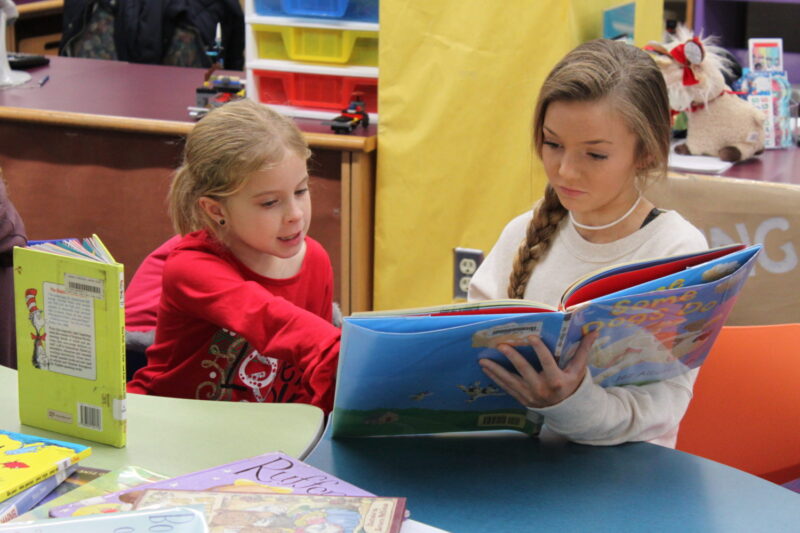 An older elementary student reads with a younger student at a desk as an example of read across america activities