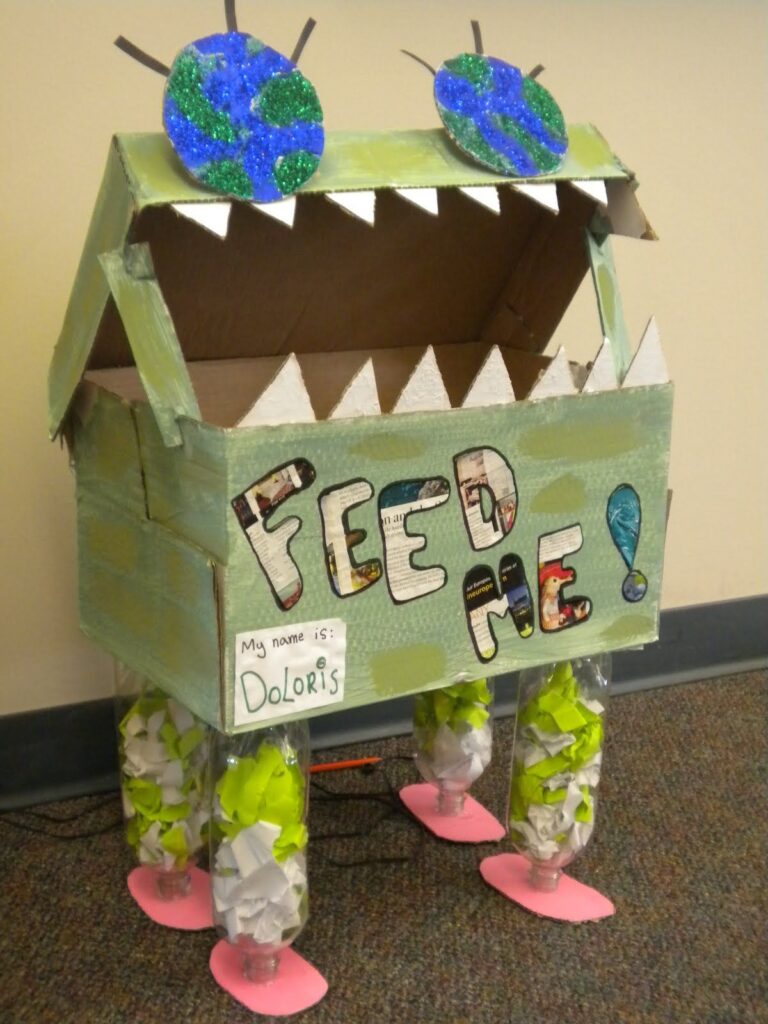 green paper recycling bin decorated with earth eyes and teeth. reads feed me on the side 