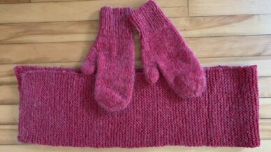 pair of knitted red mittens and scarf on wood floor
