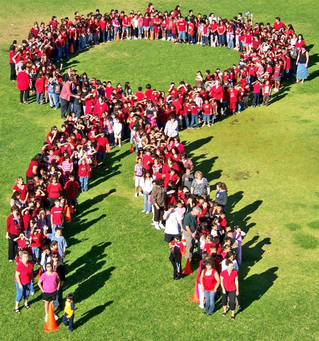 Students and teachers wearing red posing in the shape of a red ribbon, photographed from above 
