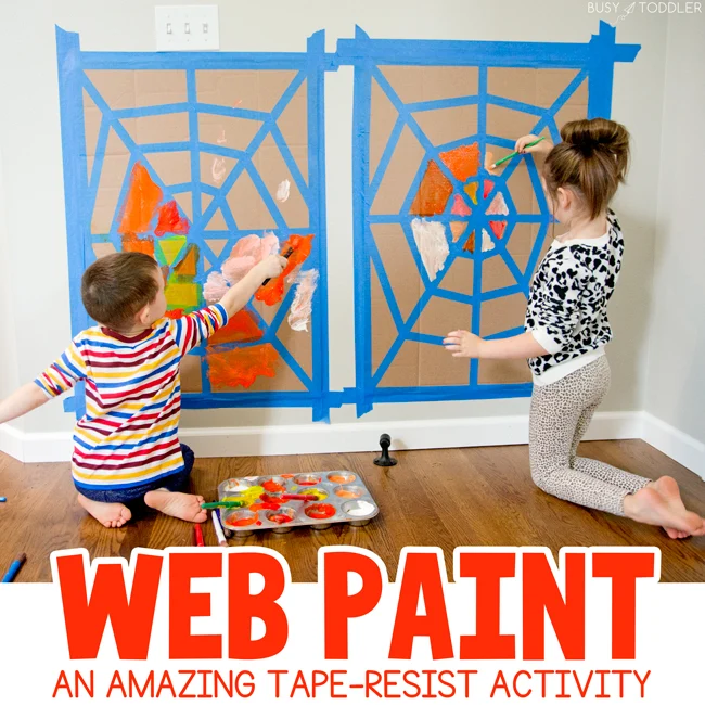 Two kids are painting cardboard that is taped to the wall. A spider web shape has been laid out using painter's tape.