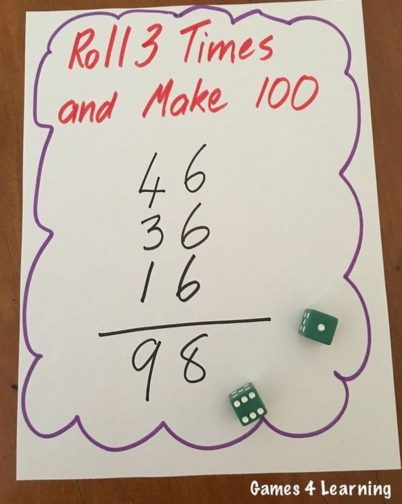 Whiteboard with a pair of dice. Text on board reads Roll 3 and Make 100, followed by a sum of 46+36+16=98. 