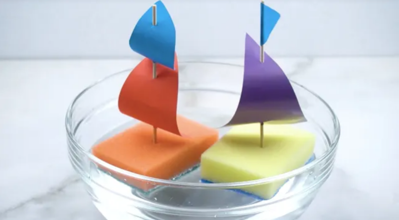 Two sailboats are constructed from sponges, toothpicks, and paper as sails. They are seen floating in a bowl of water (second grade art)