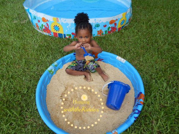 Kiddie pool games don't have to involve water like this little girl sitting in a kiddie pool that has been filled with sand and sand toys.