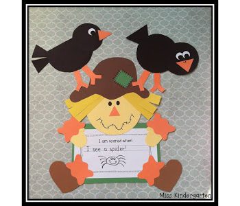 A close up of a scarecrow with two crows on its shoulders is shown holding a student's writing prompt.