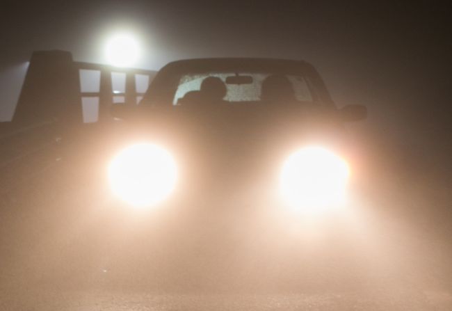 Closeup of car headlights at night with a full moon behind, illustrating Drive of Danger, one of the most well-known scary campfire stories