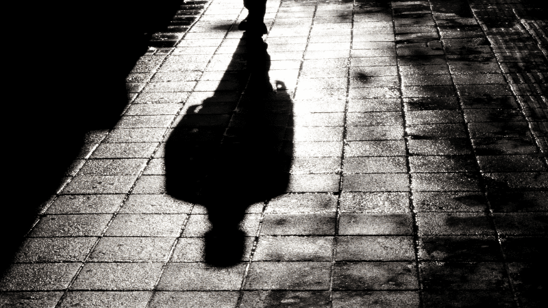 Shadow of a man walking on a city street alone at night