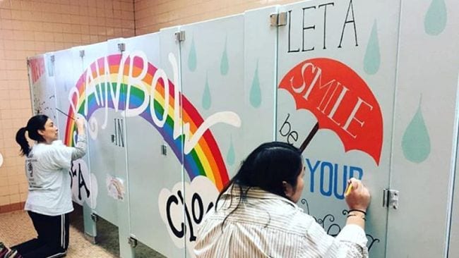 Two parents painting a mural on school bathroom doors