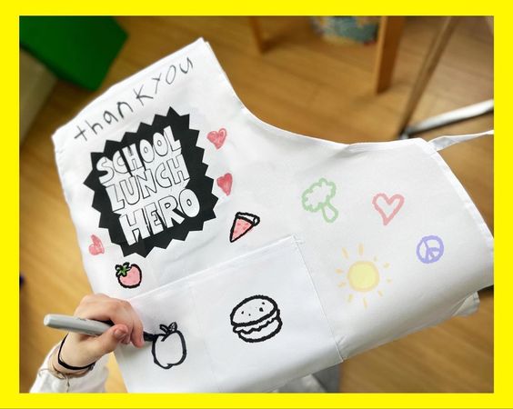 white apron that is decorated with drawings in marker for school lunch hero day 2024 