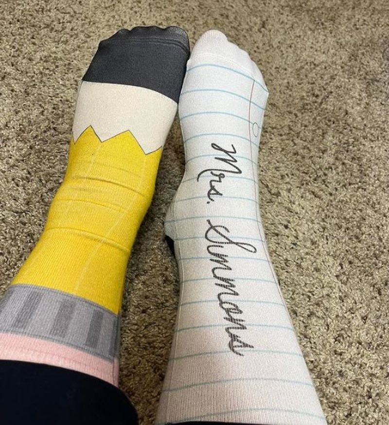 Woman wearing one sock that looks like a pencil and the other that looks like notebook paper with her name written on it