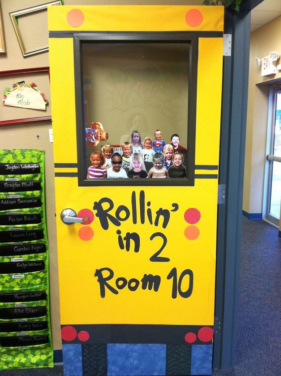 A bulletin board shows the front of a yellow school bus with the words "Rollin in 2 Room 10" The window of the school bus has photos of all of the students in the class. 