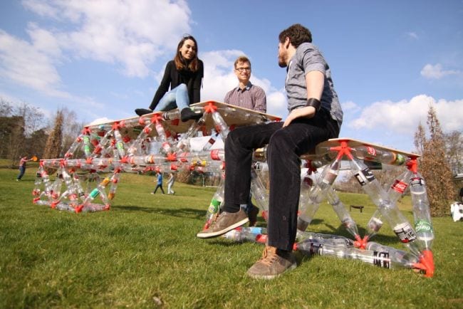 Students sitting on a large bridge made of plastic bottles