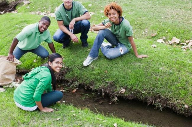 Students examining the water in a ditch in a green field (Science Experiments for High School)