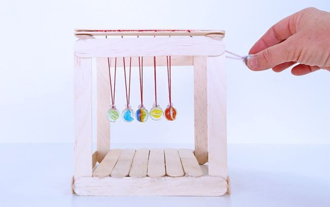 Student swinging the right ball on a DIY Newton's Cradle made of popsicle sticks and marbles