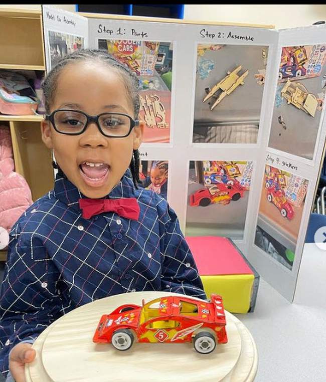 Young student holding a model car in front of their science fair project board