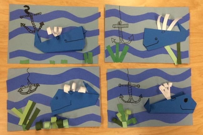 Paper origami whales on a blue construction paper background