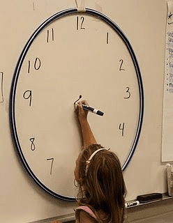 Second grader drawing clock on whiteboard. Example of activities for teaching second grade.