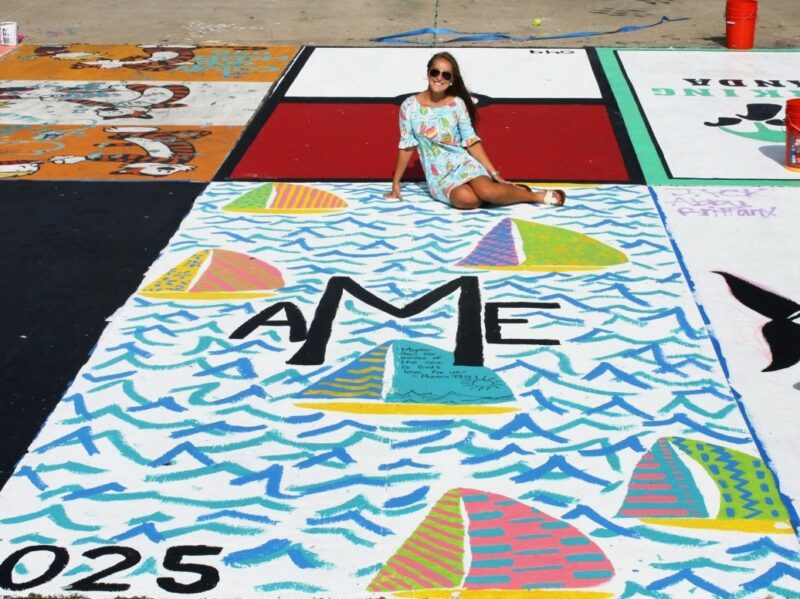 A senior in high school sitting in her decorated designated parking spot