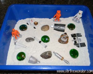 Space activities for kids can include sensory activities like this blue bin filled with white sand and space themed items.