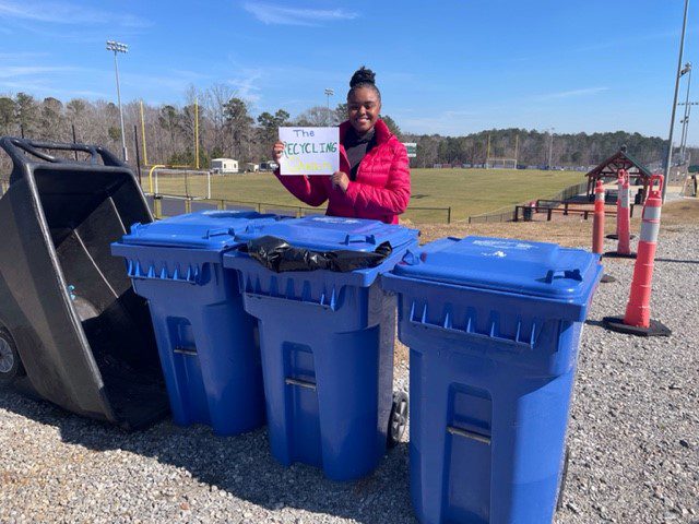 Student standing with recycling bins