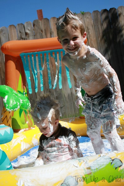 Kiddie pool games can involve sensory fun like this kiddie pool filled with shaving cream. Two kids are seen playing in it while covered in shaving cream.