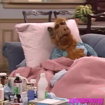 Gif of a puppet sick in bed, sneezing into a tissue.